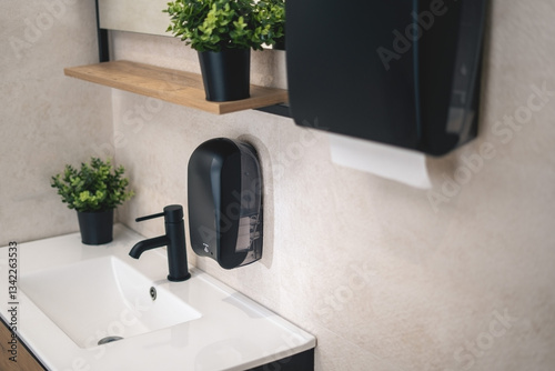 Premium black dispenser for electronic liquid soap and dispenser for paper towels in a luxury bathroom.Modernly  equipped.