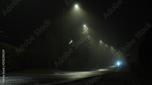 Misty street at night with glowing lamps and passing vehicles in a serene scene