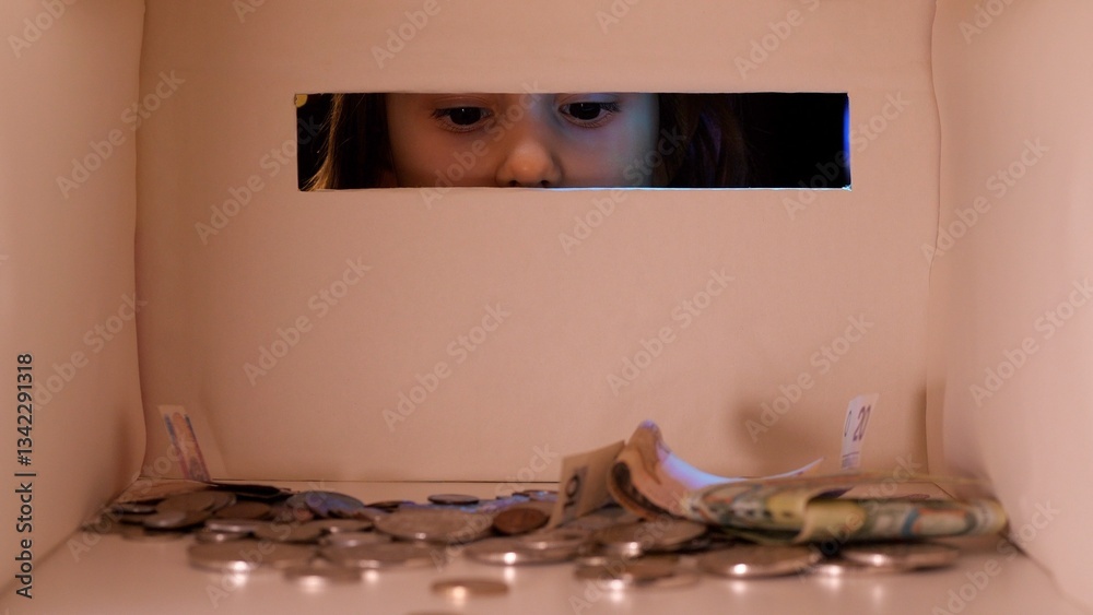 Obraz premium Young girl peers curiously through a donation box overflowing with money, reflecting hope and kindness in times of need