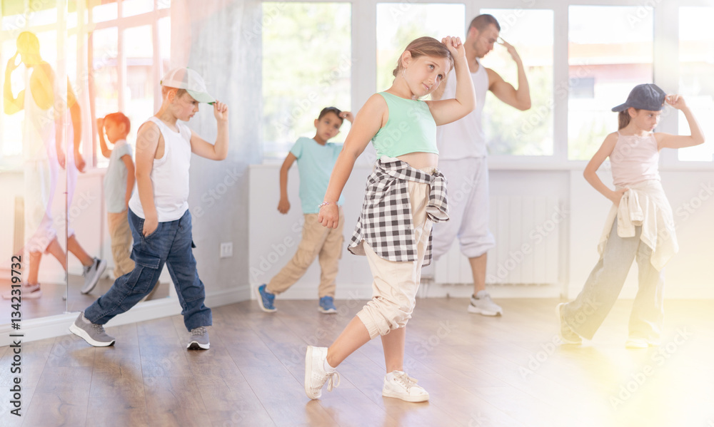 Fototapeta premium Emotional tween girl dancer rehearsing modern krump dance moves during group workout in kids studio under guidance of male instructor
