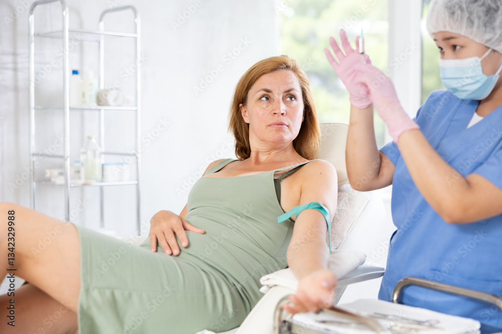 Fototapeta premium Anesthesiologist doctor injecting pain medication into vein of woman before starting surgery in a cosmetology clinic