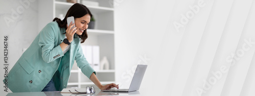 Busy happy young european woman in suit typing on laptop, calling by phone in modern office interior. Businesswoman, multitasking and business, work, lifestyle, client communication photo