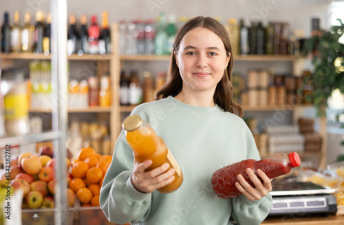 While shopping in grocery store, teen girl buyer choosing juice. Client look package of fruit drink, inspect product, reflect before buying. Customer doubt before purchase. photo