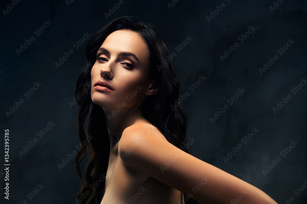 Fototapeta premium Elegant young woman with dark hair posing against a dark background, displaying natural beauty and a stylish allure.