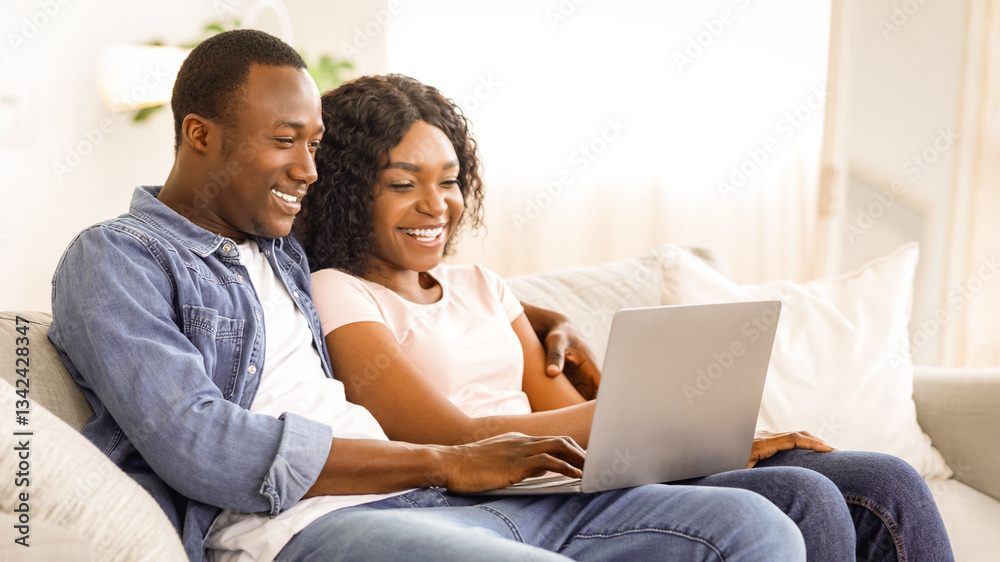 Cheerful black couple using laptop while resting on couch at living room at home, watching funny content together, copy space Cheerful black couple using laptop while resting on couch at living room at home, watching funny content together, copy space