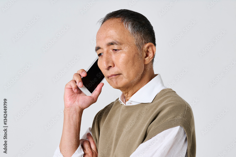 スマートフォンで通話をする暗い表情のシニア男性
