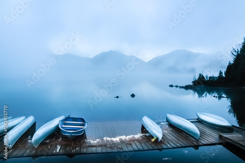 Misty Adirondack lake at dawn with canoes on dock and mountains in background