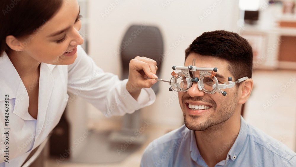 Fototapeta premium A smiling man is undergoing an eye examination in a well-lit clinic. An optometrist adjusts his glasses for clarity, ensuring an accurate assessment of his vision.