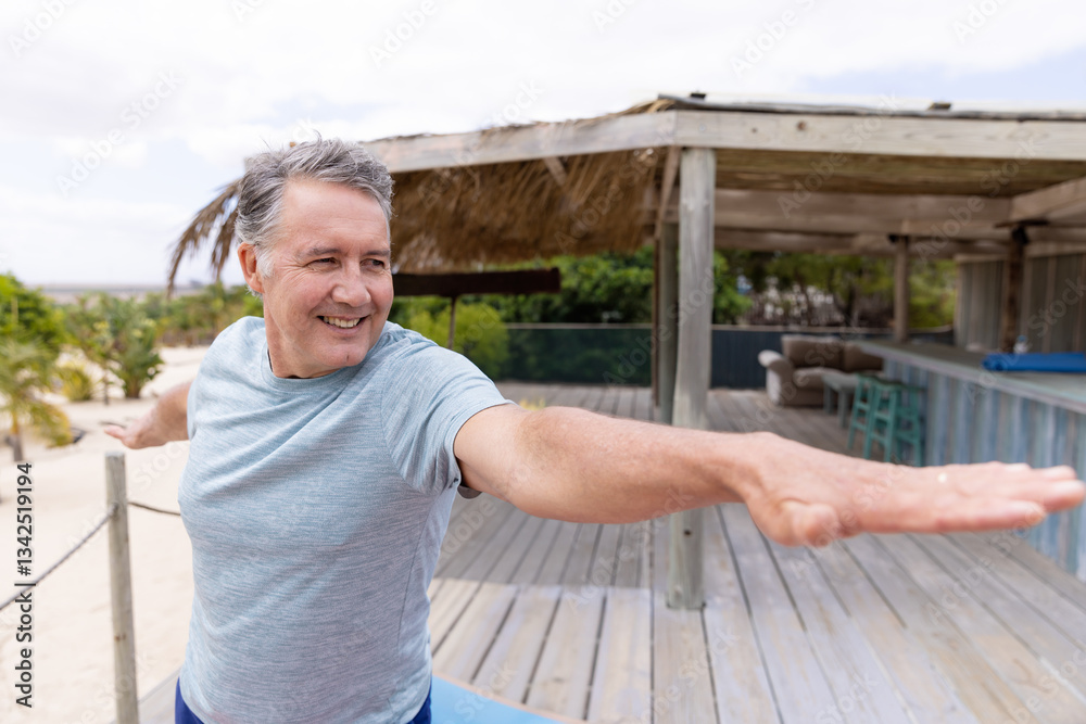 Fototapeta premium Smiling man practicing yoga on wooden deck at beachside retreat, copy space