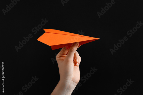 Woman with orange paper plane on black background, closeup