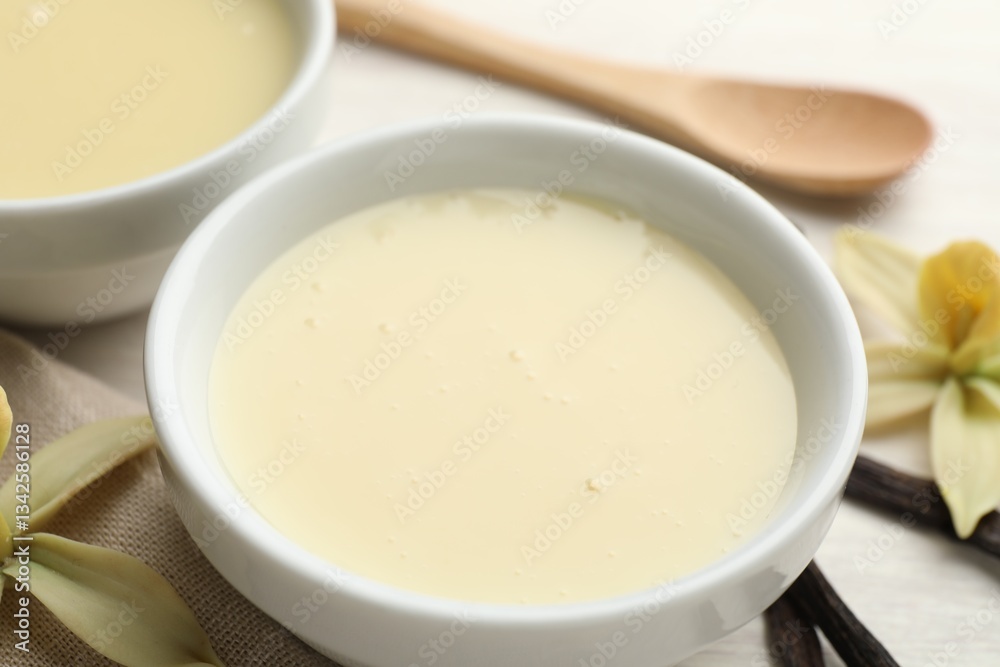 Tasty condensed milk, vanilla pods, flowers and spoon on white table, closeup Tasty condensed milk, vanilla pods, flowers and spoon on white table, closeup