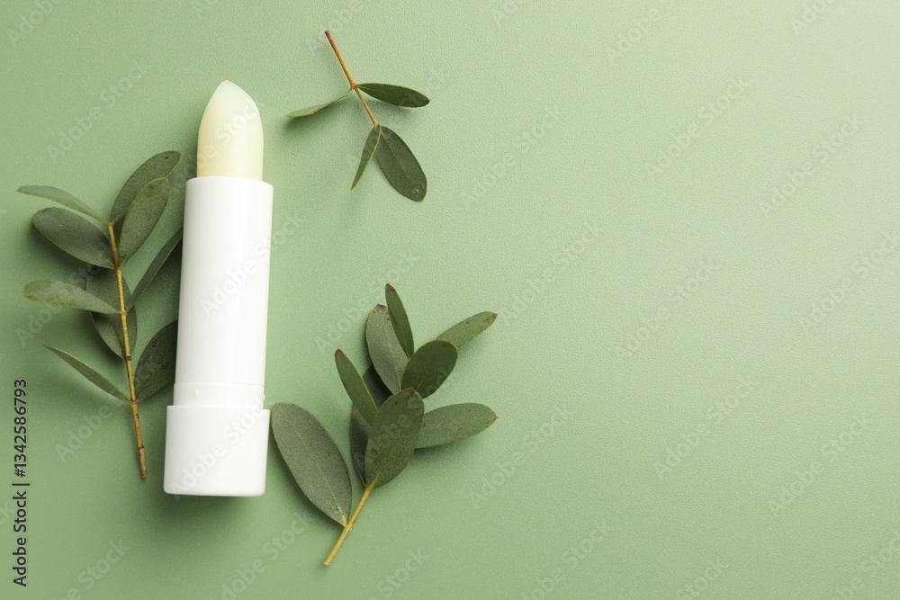 Fototapeta premium Lip balm and eucalyptus leaves on light green background, flat lay. Space for text