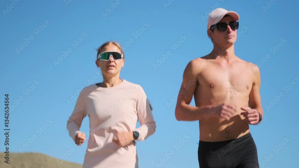Running down a barren desert road under the scorching sun, amid the heat, a pair of professional athletes move in sync. The shirtless man and the woman in a long sleeve, both athletic. Running down a barren desert road under the scorching sun, amid the heat, a pair of professional athletes move in sync. The shirtless man and the woman in a long sleeve, both athletic.