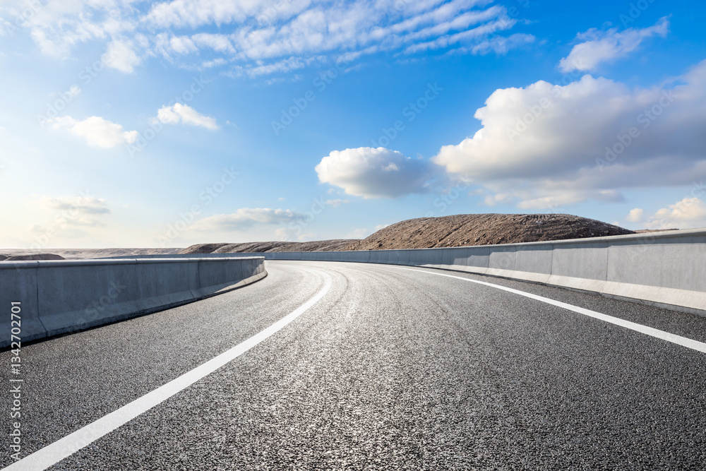 Curved asphalt road and desert dune under blue sky with white clouds