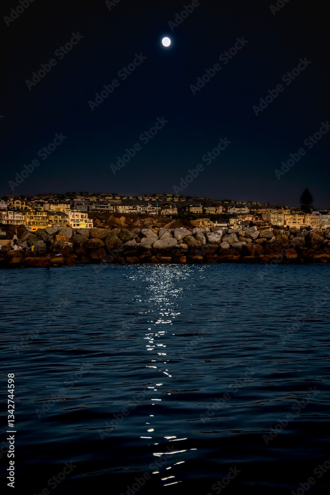 Nightfall at Newport Beach with a strong moonlight above reveals a glow-like surface of reflecting water, beach, beachfront homes and silhouette of Palm Trees