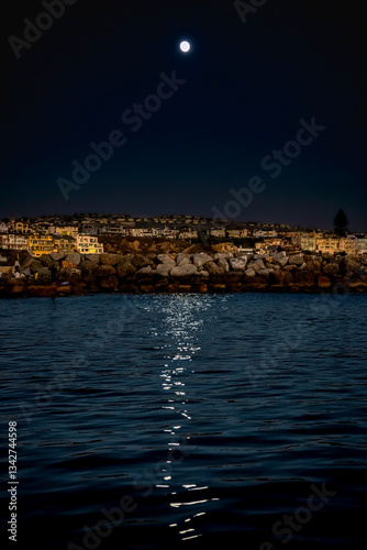 Nightfall at Newport Beach with a strong moonlight above reveals a glow-like surface of reflecting water, beach, beachfront homes and silhouette of Palm Trees 