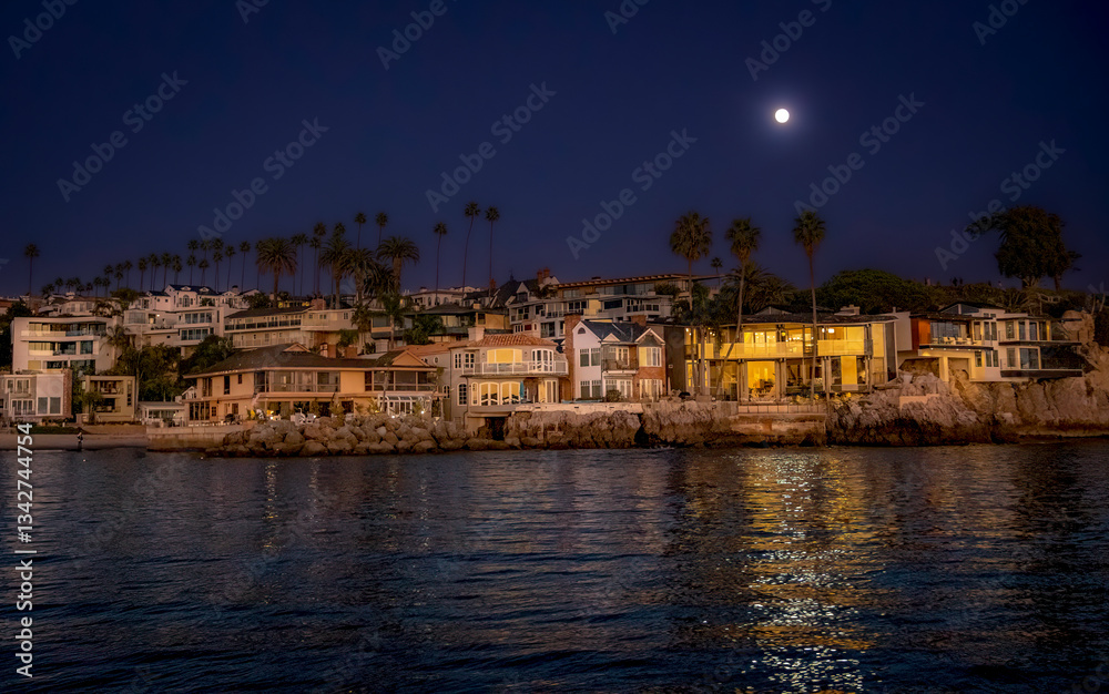 Nightfall at Newport Beach with a strong moonlight above reveals a glow-like surface of reflecting water, beach, beachfront homes and silhouette of Palm Trees