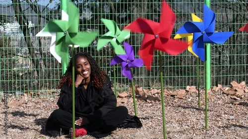 Young black woman smiling while sitting beneath colorful large windmills.