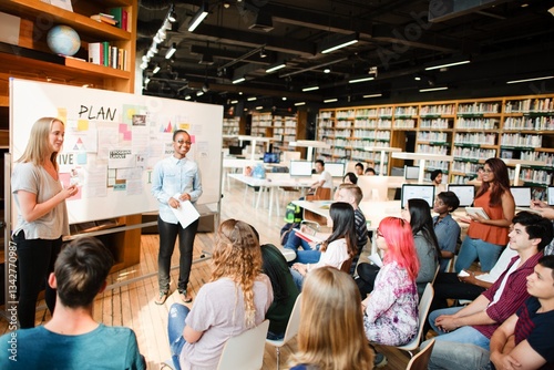 A diverse group in a library setting, with a woman presenting and a man standing by a whiteboard. Students, presentation, diverse group, learning environment. High school students presenting in class.
