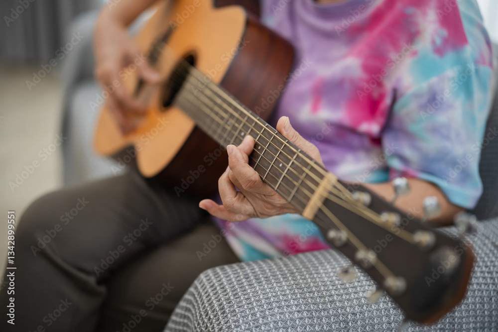 Fototapeta premium Person Playing Acoustic Guitar in Colorful Tie-Dye Shirt, Close-Up of Hands, Cozy Indoor Environment, Musician Focused on Performance
