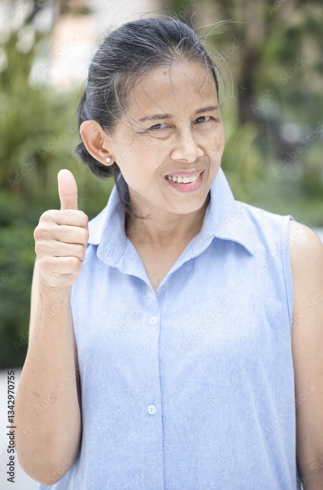 Happy smiling Asian middle aged old woman showing approving, passing, good, yes, go for it, good to go, one thumb up hand gesture Happy smiling Asian middle aged old woman showing approving, passing, good, yes, go for it, good to go, one thumb up hand gesture