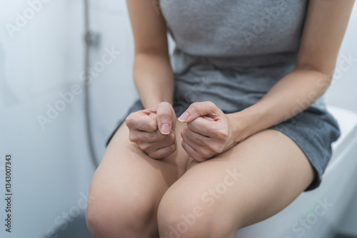 Stomach ache, urgency. Tired asian young woman holding stomach pain, pee in bathroom sitting on toilet bowl, suffer girl from urinary and incontinence. Health care of bladder, urine problem concept
