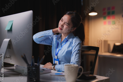 Young business woman having neck pain after long hours working on computer in office at night, suffering from office syndrome, health care and medical concept