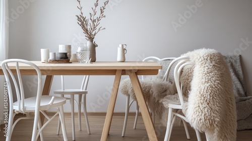 A cozy Scandinavian dining area with a light wooden table, white wishbone chairs, and a sheepskin throw draped over one seat