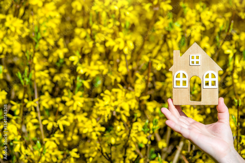 Φωτογραφία The girl holds the house symbol against the background of blossoming forsythia