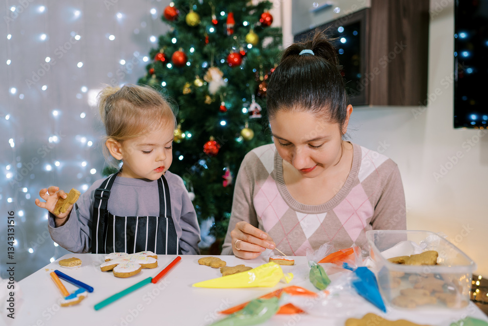 Obraz premium Little girl watching her mother painting a pattern with a toothpick on a glazed cookie