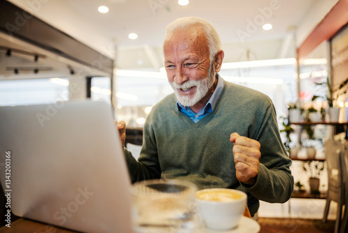 Obraz na płótnie An old man is celebrating victory and looking at laptop in coffee shop. w salonie