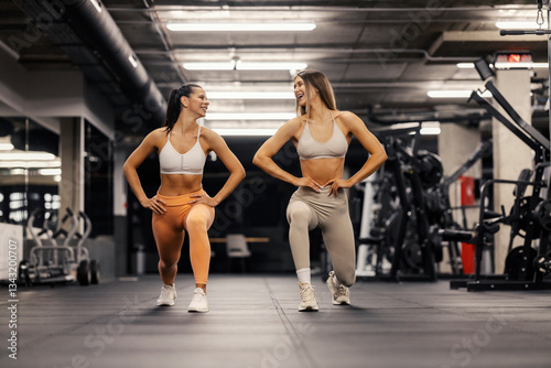 Smiling two sportswomen doing lunges at gym.
