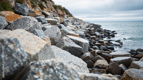 Coastal erosion barrier natural rock revetment with large boulders arranged to absorb wave energy along vulnerable shoreline during incoming tide with soft cloudy daylight