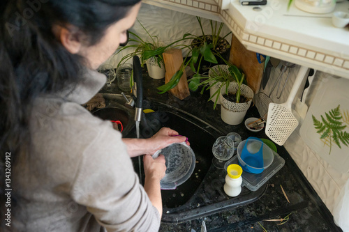 Suds in suburbia a woman tending to dish duty amidst indoor botanical bounty creates a haven of domesticity where cleanliness and serenity meet
