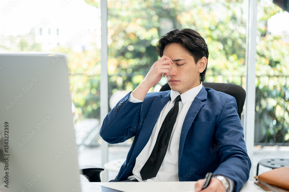 Asian businessman or male office worker is closing eyes while massaging his temples at working desk. Asian businessman or male office worker is closing eyes while massaging his temples at working desk.