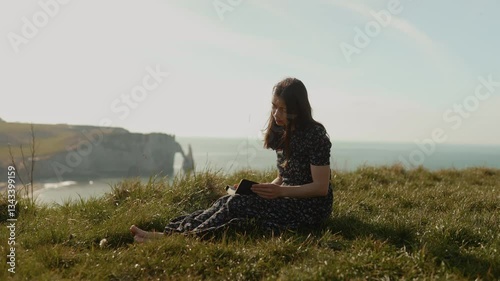 On the ocean shore in Etretat. A girl reads the Bible in the open air, gratefully looking up to the sky. A woman holds the Bible in her hands and studies the word of God on the top of a cliff. Searchi