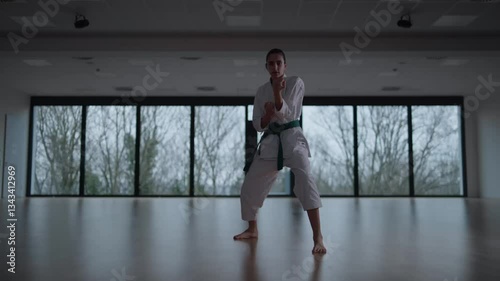 Woman training Karate in the dark, with big windows in the back