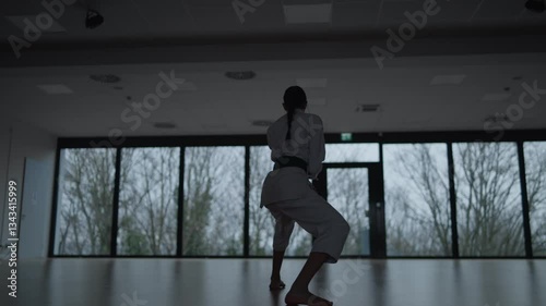 Woman training Karate in the dark, with big windows in the back