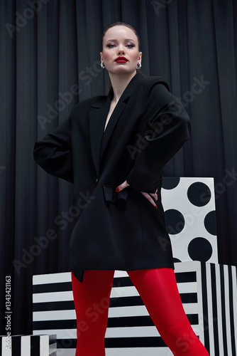 Portrait of a beautiful young woman in a black and white studio in red polntrtki and a black jacket. The model poses in a black jacket and with bright makeup. Advertising fashion and beauty.