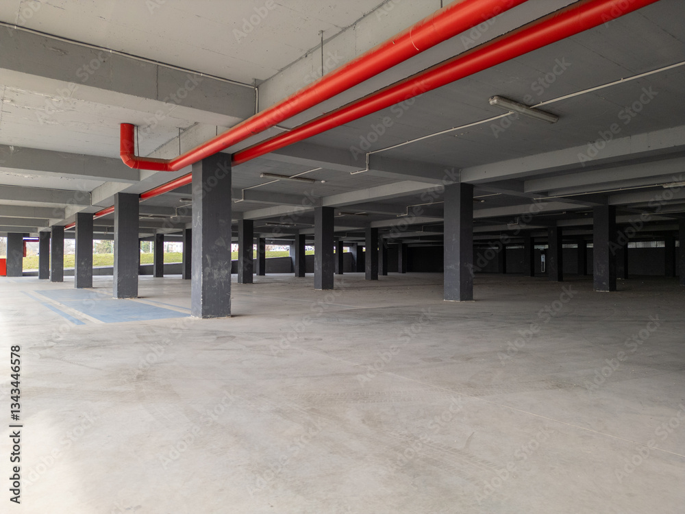 Obraz premium an empty underground parking garage with concrete pillars and open sides. The industrial space is illuminated by natural light, creating a modern yet abandoned atmosphere