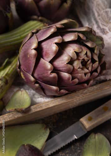 Whole purple raw roman artichokes in a wooden tray closeup. Fresh italian vegetables