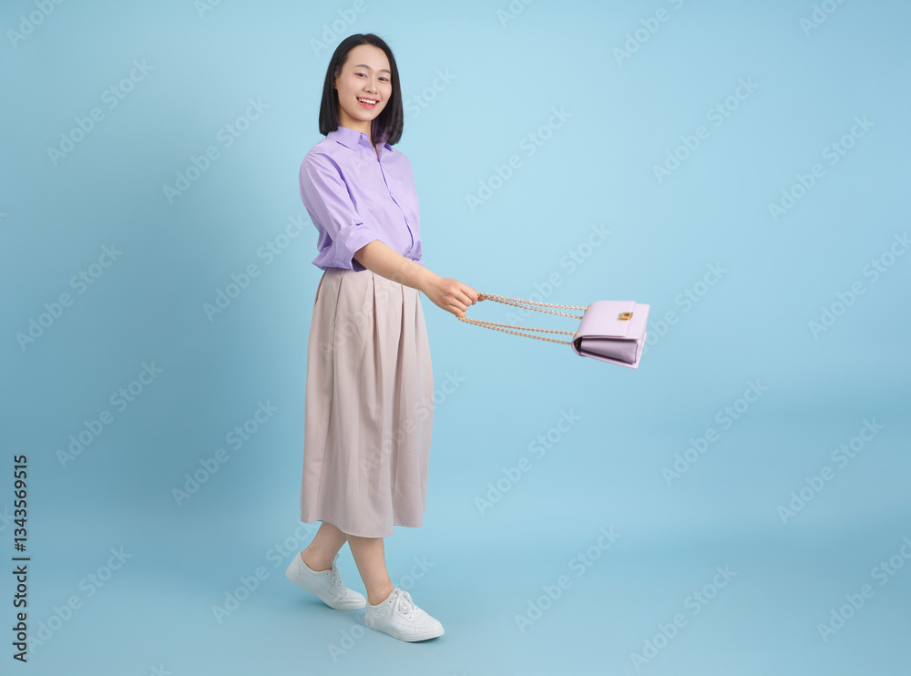 Smiling woman in pastel outfit showcasing a stylish bag against a light blue background in a cheerful indoor setting Smiling woman in pastel outfit showcasing a stylish bag against a light blue background in a cheerful indoor setting