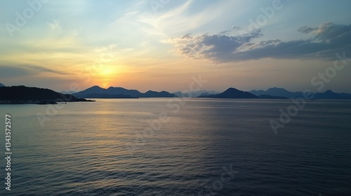 Panoramic seascape at dusk, sun sinking over island silhouettes with rippled water