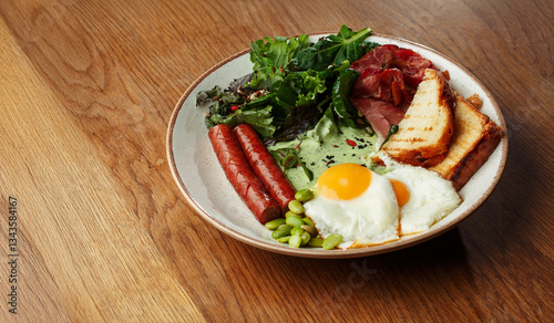 breakfast plate with fried eggs, grilled sausages, crispy bacon, toasted bread, fresh green salad. Healthy morning meal on a wooden table. copy space