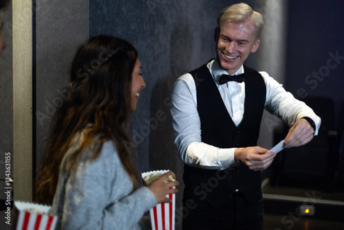 Foto Smiling usher checking tickets at movie theater entrance with young woman holdin