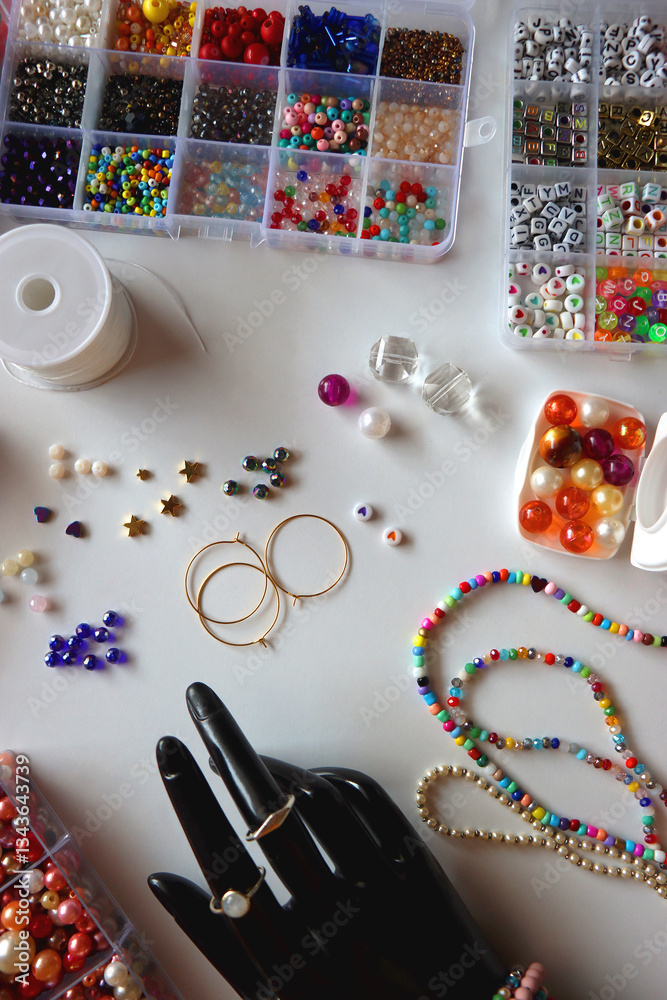 Hand figurine, colorful friendship bracelets, necklaces, various beads and DIY supplies on the table. Making jewelry at home. Flat lay.