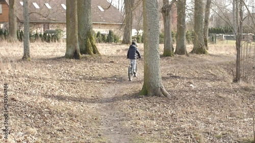 A child rides a bicycle along a quiet path lined with bare trees, creating a peaceful and seasonal atmosphere. The scene suggests adventure, independence, and outdoor exploration.