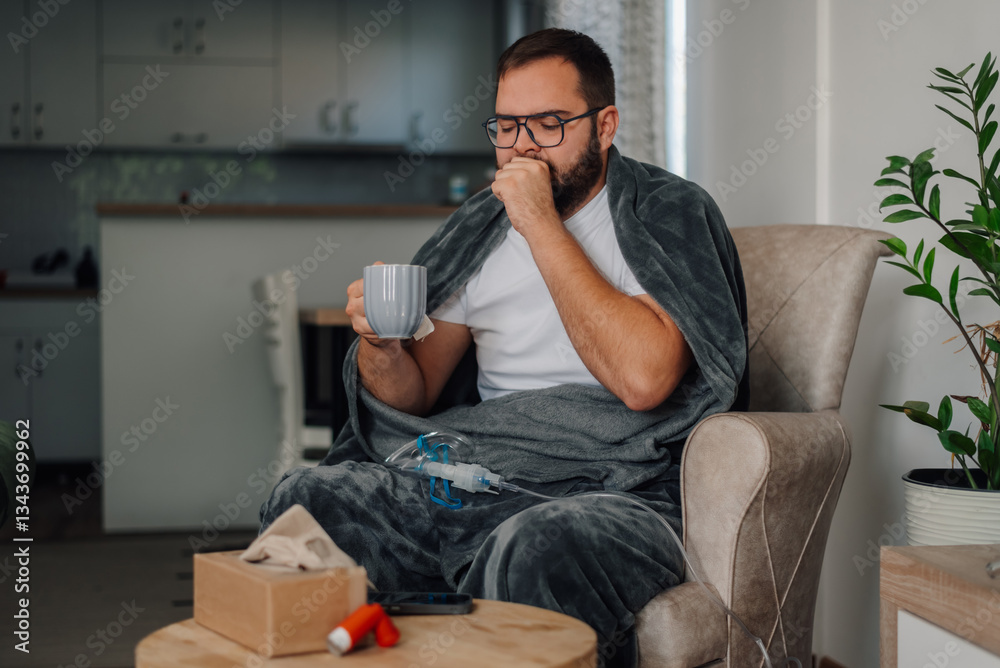 Fototapeta premium Sick man coughing at home, drinking tea and using inhaler