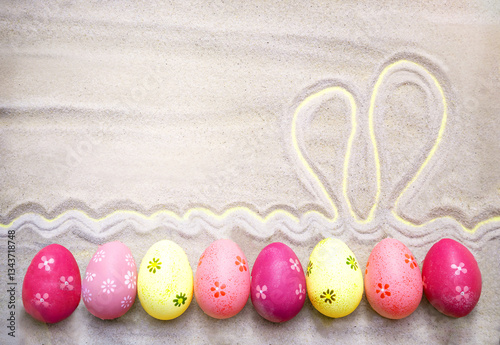 Sand texture with colorful Easter eggs and drawing rabbit's ears on the beach. Easter, spring holiday background. Empty place (pattern) for your message. Mock up, Copy space.