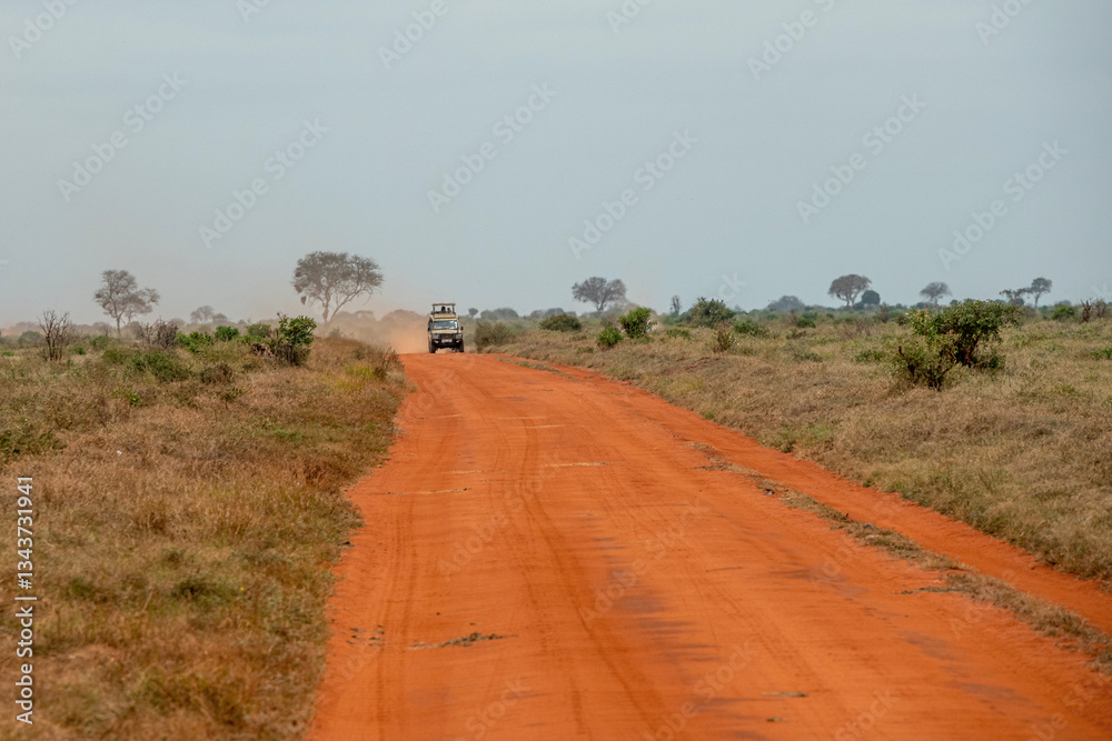 Obraz premium Jepp jadący po czerwonej drodze gruntowej biegnącej przez sawannę w Park Narodowy Tsavo i rezerwat wzgórz Taita, Kenia